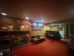 Lower-level entertainment space featuring a brick fireplace with a wood mantle, recessed ceiling lighting, a built-in wet bar with mirrored shelving, wood paneling, and a red carpeted floor - 
