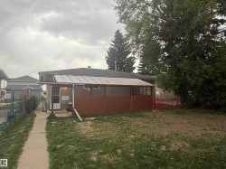 Rear exterior featuring a covered patio, paved walkway, and mature trees - 