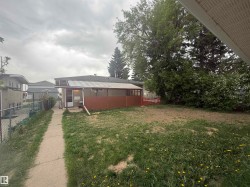 Rear exterior featuring a covered porch, an expansive lawn area, mature trees, and a concrete pathway - 