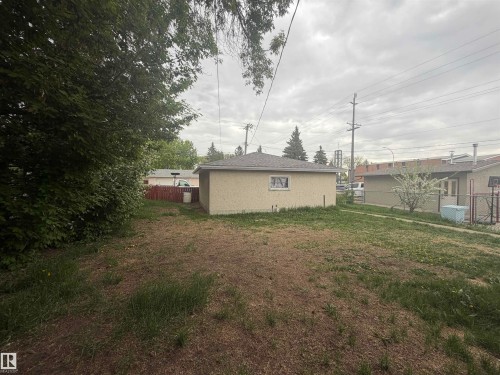 Expansive rear yard featuring a detached structure with stucco siding and a shingled roof, mature perimeter foliage, and established fencing - 13207 117 Street, Edmonton, AB 