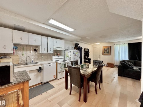 Kitchen featuring white cabinetry, tile backsplash, double basin sink, and wood-finish flooring - #29 13580 38 St Nw, Edmonton, AB - Indoor