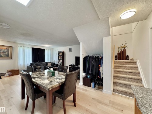 Open-concept living area featuring light wood-finish flooring, a carpeted staircase with white risers, and a flat-panel ceiling light fixture - #29 13580 38 St Nw, Edmonton, AB - Indoor Photo Showing Dining Room