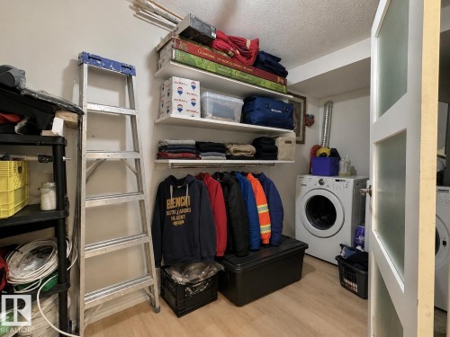 Laundry room featuring a front-loading washing machine, light wood-finish flooring, built-in shelving, and a clothing rod - #29 13580 38 St Nw, Edmonton, AB - Indoor Photo Showing Other Room