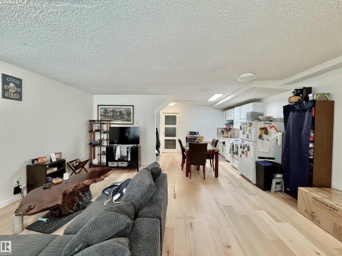 Open-concept living space featuring light wood-finish flooring, white walls, and a recessed kitchen area with white cabinetry - #29 13580 38 St Nw, Edmonton, AB - Indoor Photo Showing Living Room