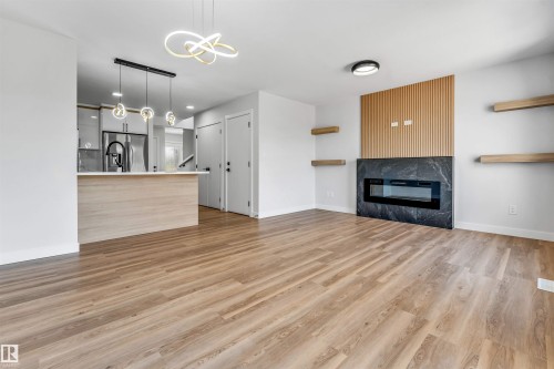 Open-concept living space featuring wood-finish flooring, a contemporary fireplace with a dark stone surround, and a slatted wood accent wall - 1712 27 St Nw, Edmonton, AB - Indoor Photo Showing Other Room With Fireplace