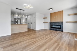 Open-concept living space featuring wood-finish flooring, a contemporary fireplace with a dark stone surround, and a slatted wood accent wall - 