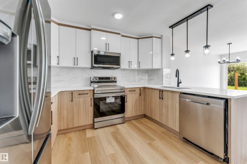 Modern kitchen featuring two-tone cabinetry, stainless steel appliances, a white countertop, and wood-finish flooring - 1714 27 St. Nw, Edmonton, AB - Indoor Photo Showing Kitchen With Upgraded Kitchen
