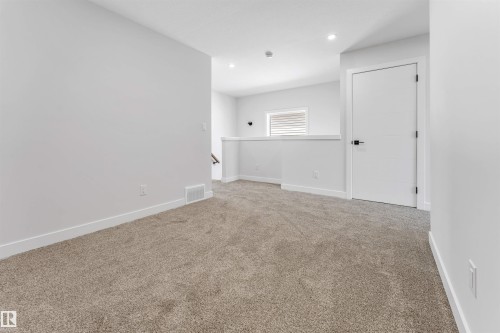 Carpeted landing area featuring recessed lighting, a contemporary white door with matte black hardware, and a window with horizontal blinds - 1714 27 St. Nw, Edmonton, AB - Indoor Photo Showing Other Room