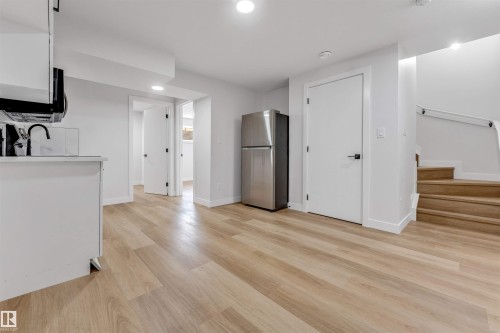 Open-concept living space featuring wood-finish flooring, white walls, recessed lighting, and a modern staircase with a white handrail - 1714 27 St. Nw, Edmonton, AB - Indoor