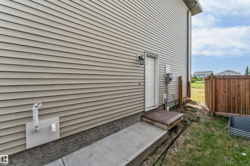 Exterior siding with a white entry door and a wooden step leading to a concrete walkway - 1714 27 St. Nw, Edmonton, AB - Outdoor With Exterior