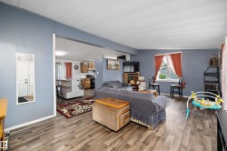 Open-concept living area featuring wood-finish flooring, a wall-mounted mirror, and a kitchen visible in the background - 