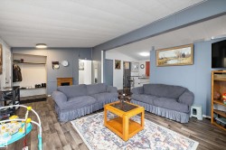 Spacious living area featuring wood-finish flooring, a contemporary ceiling light fixture, and a decorative fireplace surround - 