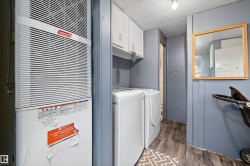 Dedicated utility area featuring a central air unit, side-by-side washer and dryer, upper cabinetry, and wood-finish flooring - 