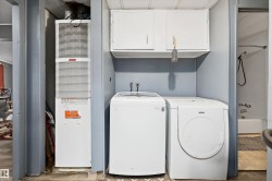 Dedicated utility area featuring a stacked washer and dryer, upper cabinetry, and a full HVAC unit - 