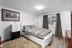 Bedroom featuring wood-finish flooring, white walls, and a window with dark drapery - 