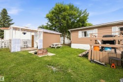 Grassed backyard with a wood deck, a covered patio structure, a freestanding shed, a picnic table, and a fire pit area - 