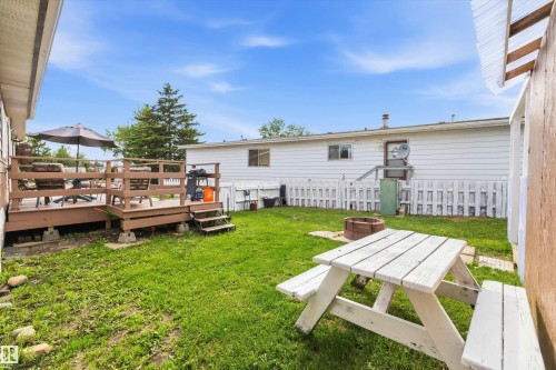 Expansive backyard featuring a multi-level wood deck with railing, a white picket fence, a built-in fire pit, and a grassy lawn area - 46 Maple Terrace Northwest, Edmonton, AB - Outdoor With Deck Patio Veranda With Exterior