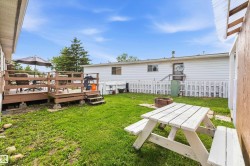 Expansive backyard featuring a multi-level wood deck with railing, a white picket fence, a built-in fire pit, and a grassy lawn area - 