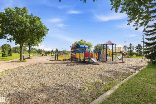 Community playground featuring colorful structures with slides, climbing elements, and a wood chip ground cover - 46 Maple Terrace Northwest, Edmonton, AB - Outdoor