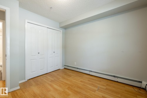 Room featuring wood-finish flooring, light-colored walls, and a white bi-fold closet with panel detailing - #103 12838 65 St Nw Nw, Edmonton, AB - Indoor Photo Showing Other Room