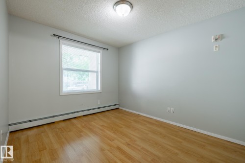Room with wood-finish flooring, light gray walls, a white window frame, and baseboard heating - #103 12838 65 St Nw Nw, Edmonton, AB - Indoor Photo Showing Other Room