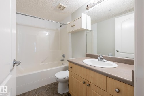 Bathroom featuring a full tub and shower combination, wood-finish vanity with an integrated sink, broad countertop, and mirrored wall - #103 12838 65 St Nw Nw, Edmonton, AB - Indoor Photo Showing Bathroom
