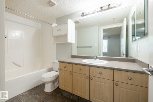Bathroom featuring a single vanity with wood-finish cabinetry and a neutral countertop - #103 12838 65 St Nw Nw, Edmonton, AB - Indoor Photo Showing Bathroom