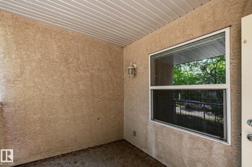 Exterior patio featuring a textured stucco finish, white vinyl window, and a wall-mounted outdoor light fixture - #103 12838 65 St Nw Nw, Edmonton, AB - 