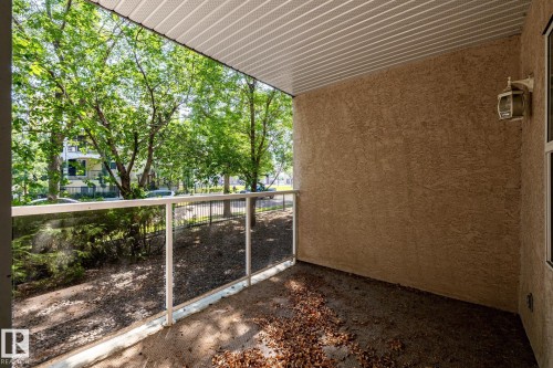 Covered balcony featuring stucco exterior, a glass panel railing, and a textured ceiling - #103 12838 65 St Nw Nw, Edmonton, AB - Outdoor