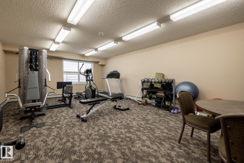 Fitness room featuring patterned carpet, a window, and fluorescent lighting - #103 12838 65 St Nw Nw, Edmonton, AB - Indoor Photo Showing Gym Room