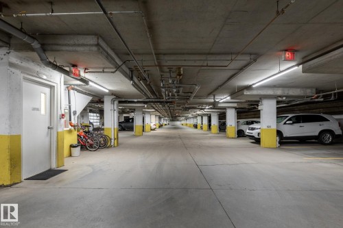 Underground concrete parking garage featuring ample vehicle spaces, exposed ceiling utilities, and bright overhead strip lighting - #103 12838 65 St Nw Nw, Edmonton, AB - Indoor Photo Showing Garage