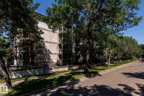 Multi-story building featuring a textured facade, multiple balconies with metal railings, and a low concrete wall with a wrought iron fence - #103 12838 65 St Nw Nw, Edmonton, AB - Outdoor