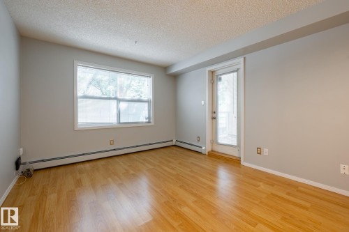 Bright room featuring wood-finish flooring, a large window, a glass-paneled door, and baseboard heating - #103 12838 65 St Nw Nw, Edmonton, AB - Indoor Photo Showing Other Room