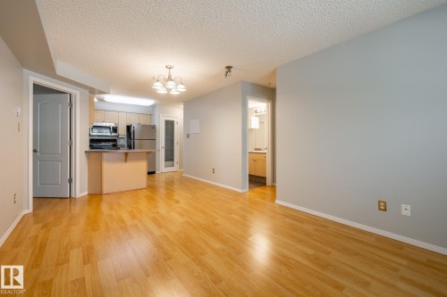 Spacious main living area featuring wood-finish flooring, light gray walls, and an open-concept kitchen - #103 12838 65 St Nw Nw, Edmonton, AB - Indoor Photo Showing Kitchen