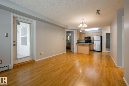 Open-concept living space featuring wood-finish flooring, a light gray color palette, and a full-light glass door - #103 12838 65 St Nw Nw, Edmonton, AB - Indoor Photo Showing Other Room