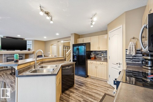 Kitchen featuring light wood-finish cabinetry, dark countertops, a mosaic tile backsplash, and stainless steel double sink - 16765 119 Street Nw, Edmonton, AB - Indoor Photo Showing Kitchen With Double Sink