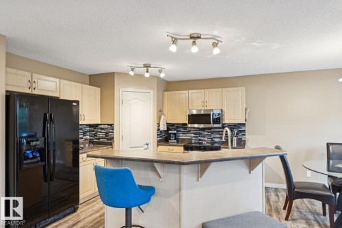 Kitchen featuring a breakfast bar, wood-finish flooring, light wood cabinetry, built-in microwave, and track lighting - 16765 119 Street Nw, Edmonton, AB - Indoor Photo Showing Kitchen