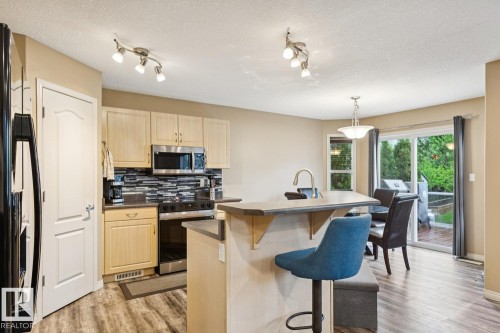 Kitchen featuring light wood-finish cabinetry, stainless steel appliances, a tiled backsplash, and an island with a built-in breakfast bar - 16765 119 Street Nw, Edmonton, AB - Indoor Photo Showing Kitchen