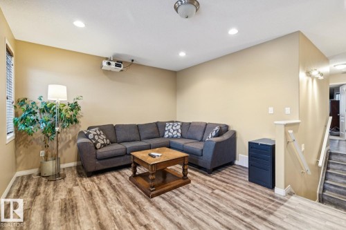 Recreation room featuring wood-finish flooring, recessed ceiling lighting, a wall-mounted projector, and a staircase with a white handrail - 16765 119 Street Nw, Edmonton, AB - Indoor