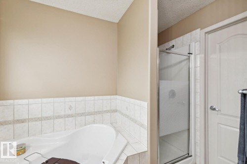 Corner soaking tub with white tile surround and decorative accent band, alongside a standing shower with a clear glass enclosure - 16765 119 Street Nw, Edmonton, AB - Indoor Photo Showing Bathroom