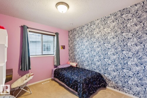 Bedroom featuring a statement wall with botanical-patterned wallpaper, flush-mount ceiling lighting, a single window with blinds, and neutral carpeting - 16765 119 Street Nw, Edmonton, AB - Indoor Photo Showing Bedroom