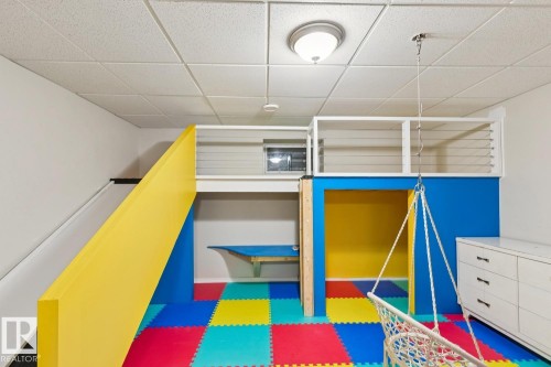 Multicolor floor padding in a recreation space featuring a built-in slide, elevated loft area with louvered railing, and a vibrant blue and yellow play structure - 16765 119 Street Nw, Edmonton, AB - Indoor