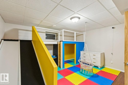 Recreational room featuring a multi-level loft structure with balustrade railing, a built-in slide, and a vibrant multi-colored floor mat - 16765 119 Street Nw, Edmonton, AB - Indoor Photo Showing Other Room