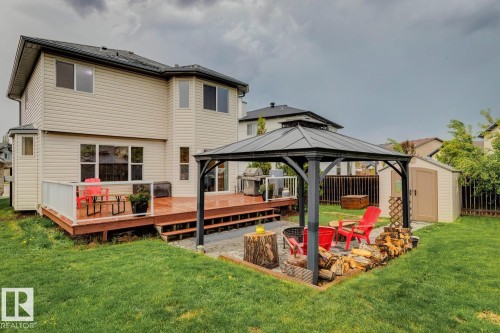 Expansive backyard featuring a wood deck with glass railing, a gazebo over a paver patio with a built-in fire pit, a storage shed, and a privacy fence - 16765 119 Street Nw, Edmonton, AB - Outdoor With Deck Patio Veranda
