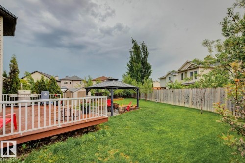 Expansive backyard featuring a wood-finish deck with white railings, a manicured lawn, a gray metal gazebo, and a wood privacy fence - 16765 119 Street Nw, Edmonton, AB - Outdoor With Deck Patio Veranda