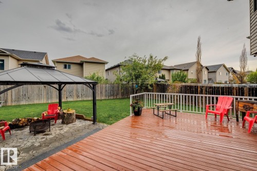 Expansive backyard featuring a wood-finish deck with white railing, a stone patio with a fire pit, and a black gazebo with a hardtop roof - 16765 119 Street Nw, Edmonton, AB - Outdoor With Deck Patio Veranda With Exterior