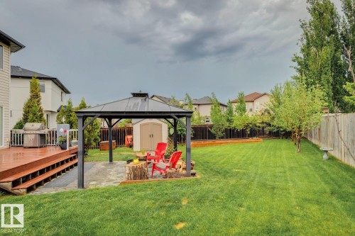 Expansive backyard featuring a large wood-finish deck, a paved patio with a metal gazebo, a storage shed, a lush green lawn, and mature trees along the perimeter - 16765 119 Street Nw, Edmonton, AB - Outdoor With Deck Patio Veranda With Backyard