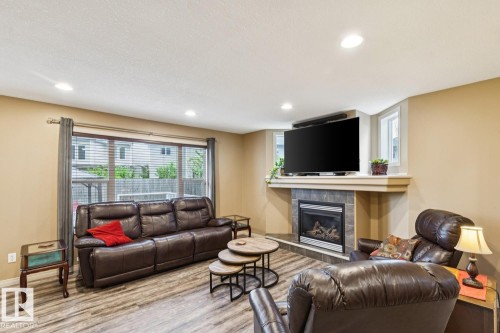 Living area featuring wood-finish flooring, recessed lighting, a wide window with blinds, a tiled fireplace with a mantel, and two additional windows - 16765 119 Street Nw, Edmonton, AB - Indoor Photo Showing Living Room With Fireplace