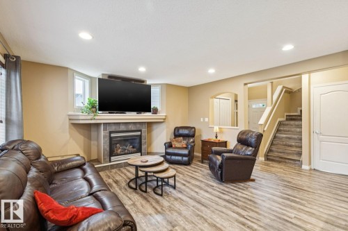 Living area featuring wood-finish flooring, a corner fireplace with a tile surround and mantel, recessed lighting, and a staircase with wood-finish treads and white risers - 16765 119 Street Nw, Edmonton, AB - Indoor Photo Showing Living Room With Fireplace