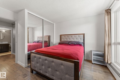 Bedroom featuring wood-finish flooring, a mirrored closet, and a large window with vertical blinds - #503 10175 114 St Nw, Edmonton, AB - Indoor Photo Showing Bedroom